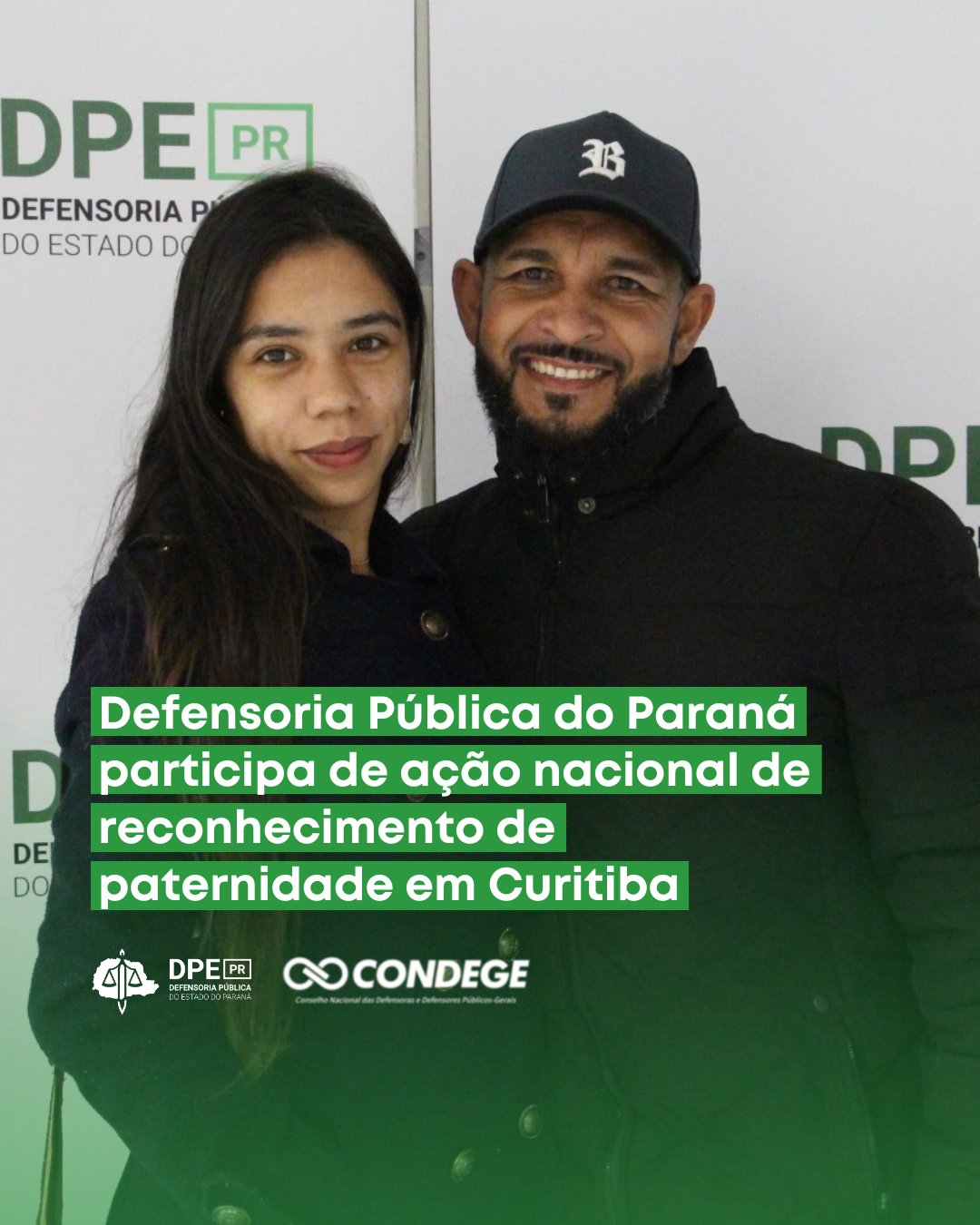 A imagem mostra pai e filha socioafetivos em frente a um painel com o nome e o logotipo da Defensoria. Ambos sorriem para a foto e estão próximos um do outro, em uma posição de proximidade e afeto.