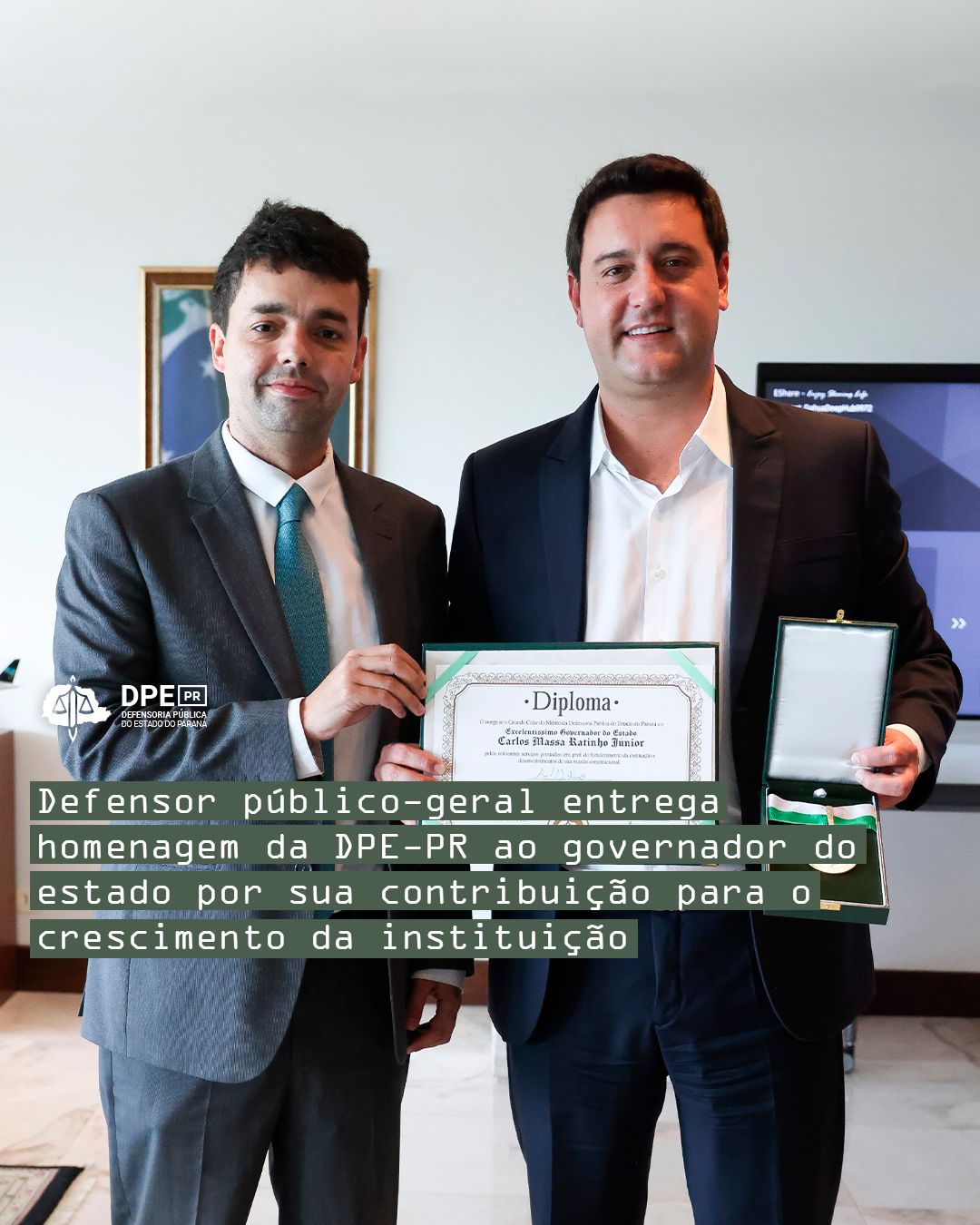 Imagem com a foto do Defensor Público-Geral, André Giamberardino, entregando ao governador do estado do Paraná, Carlos Massa Ratinho Junior, um certificado e uma medalha de homenagem pela colaboração com o crescimento da Defensoria. Os dois são homens caucasianos altos e com cabelos castanhos. Ambos usam terno e gravata. Alinhado à esquerda, o título da matéria, tarjado em verde e, acima, o logo da Defensoria em branco.