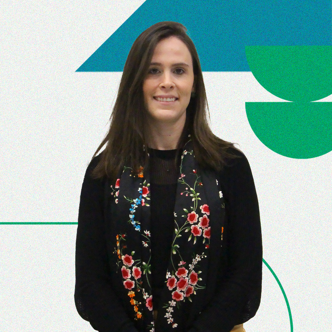 Imagem com a foto da segunda subdefensora pública-geral, Thaisa Oliveira. Ela é uma mulher branca de cabelos castanhos e usa uma camiseta de manga longa preta com um lenço florido em seu pescoço.