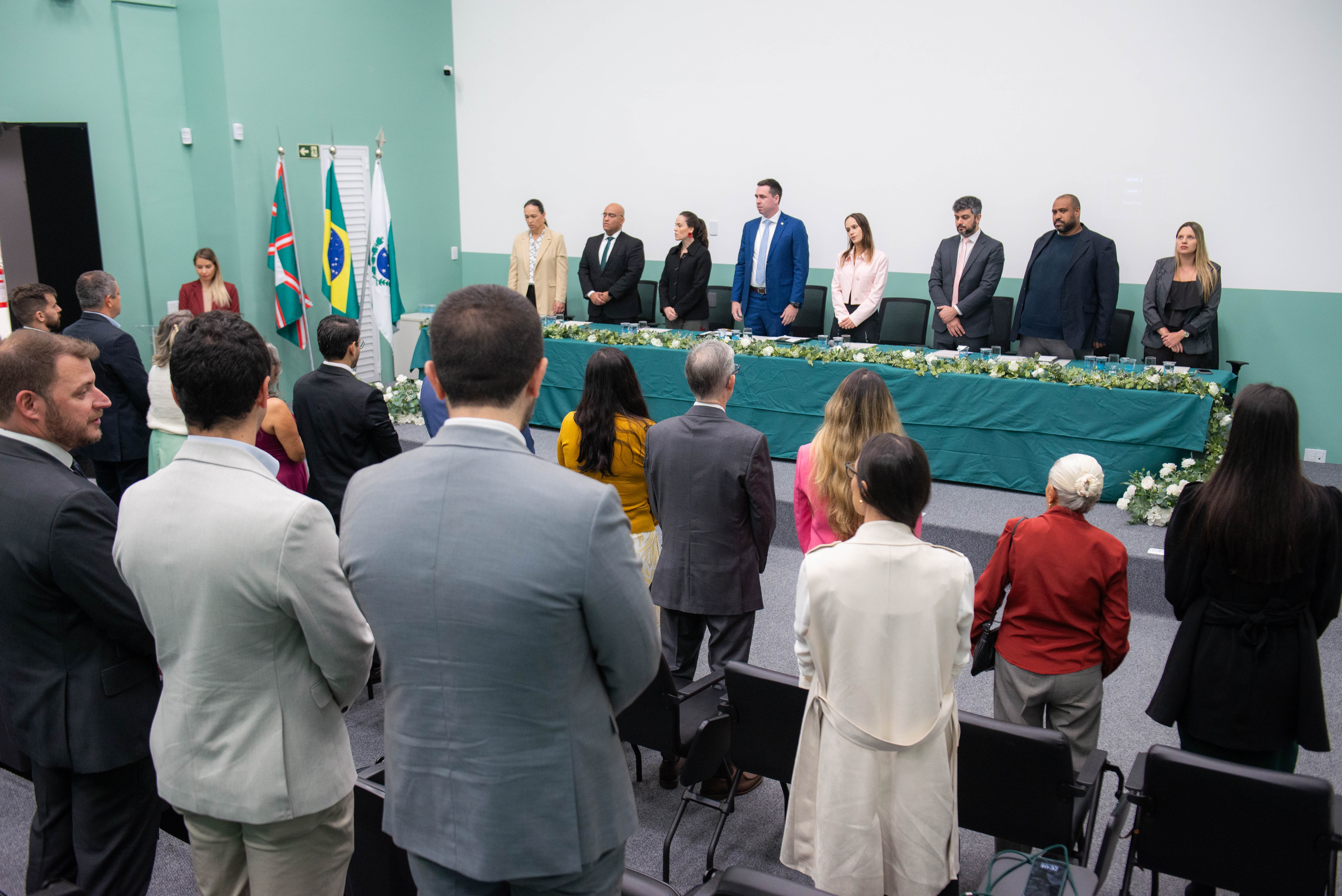 Imagem horizontal colorida onde se vê o público em primeiro plano e ao fundo a mesa de representantes da instituição que conduziram a cerimônia de posse dos novos Defensores Públicos do Paraná.