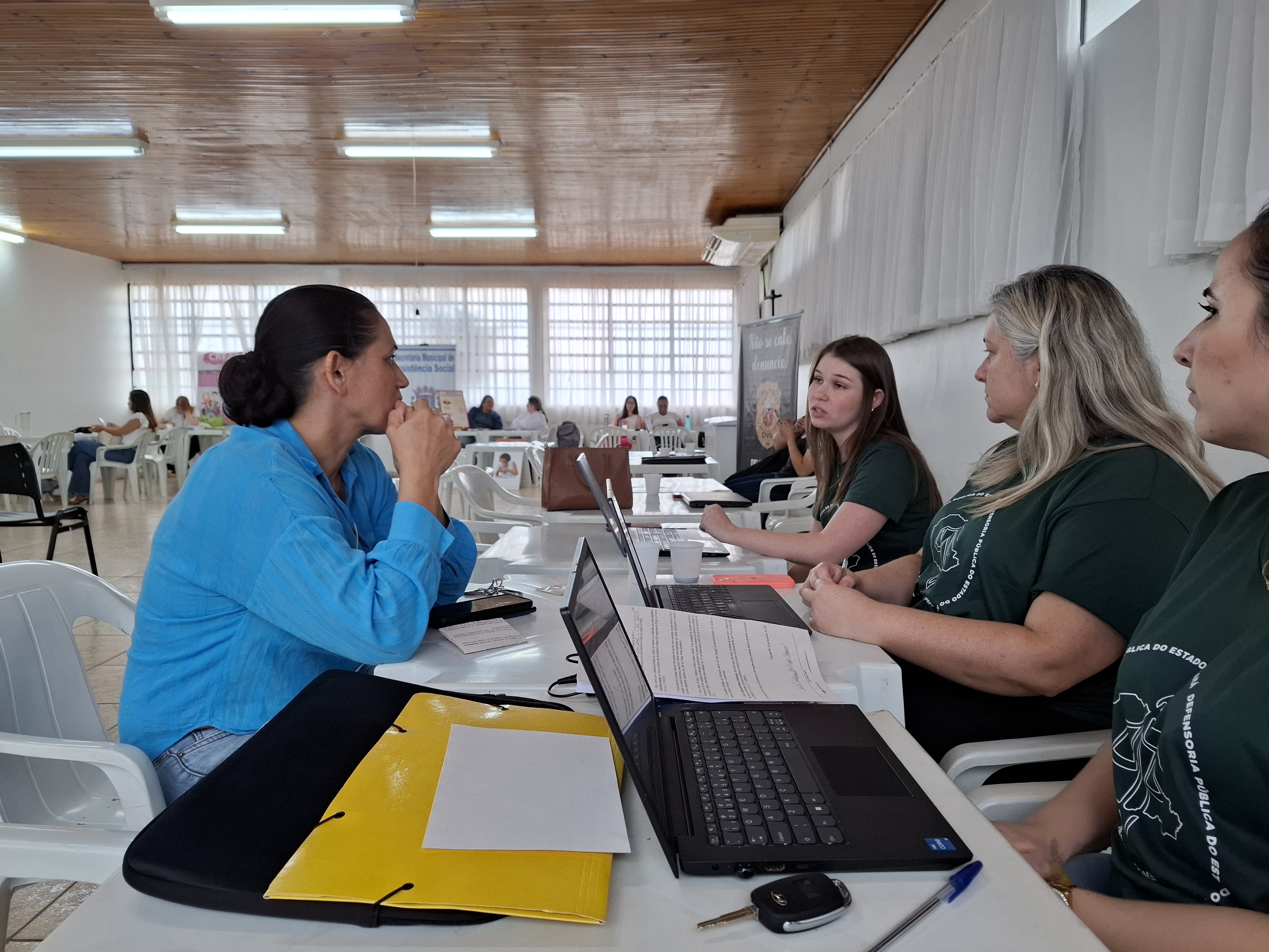 Imagem que mostra um dos atendimentos do evento. Três pessoas da Defensoria atendem uma mulher que escuta orientações delas.