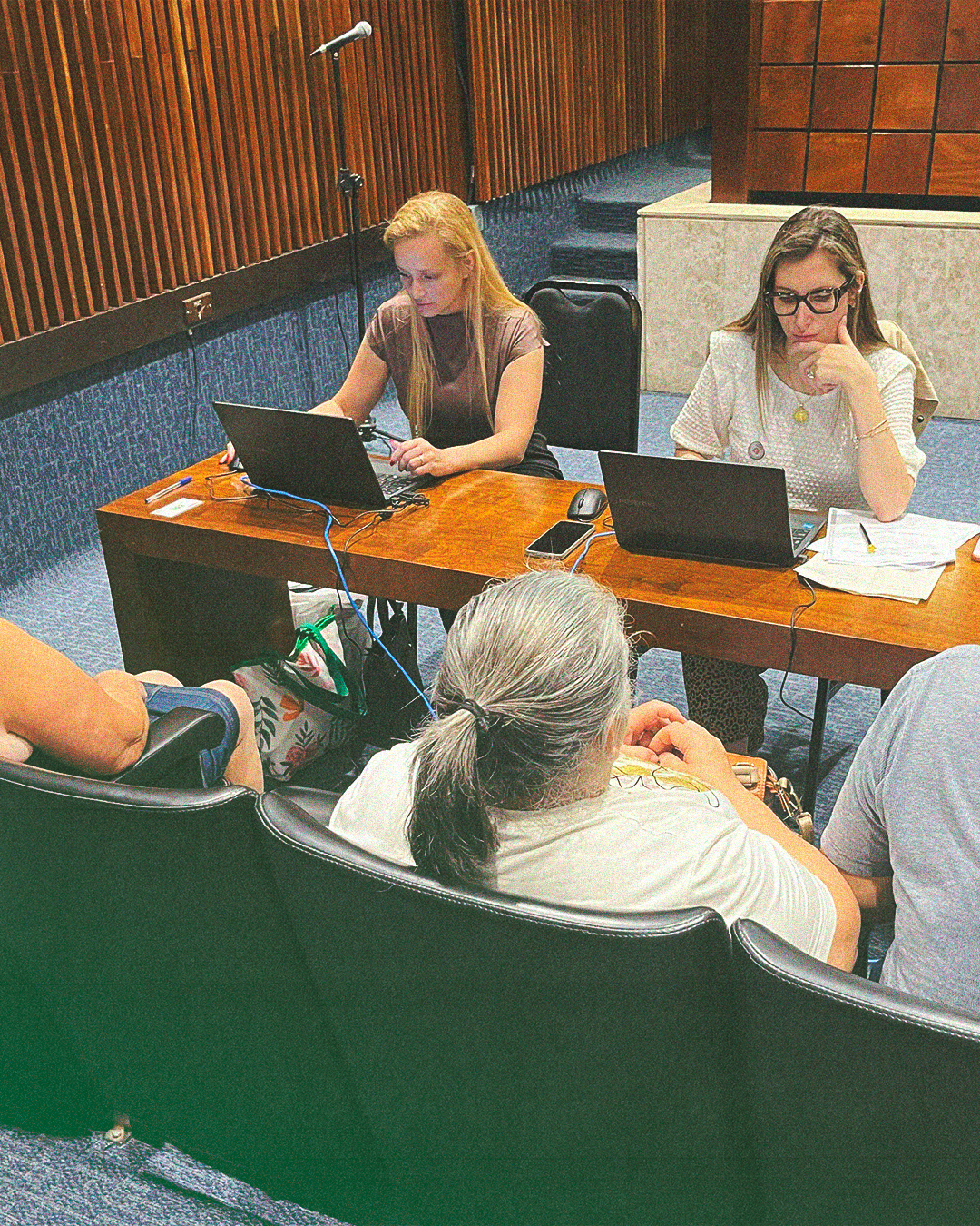Imagem de uma foto de um atendimento presencial, duas servidoras públicas estão conferindo informações em seus notebooks enquanto três usuários da Defensoria Pública aguardam. Na parte central inferior da imagem, está o título da matéria.