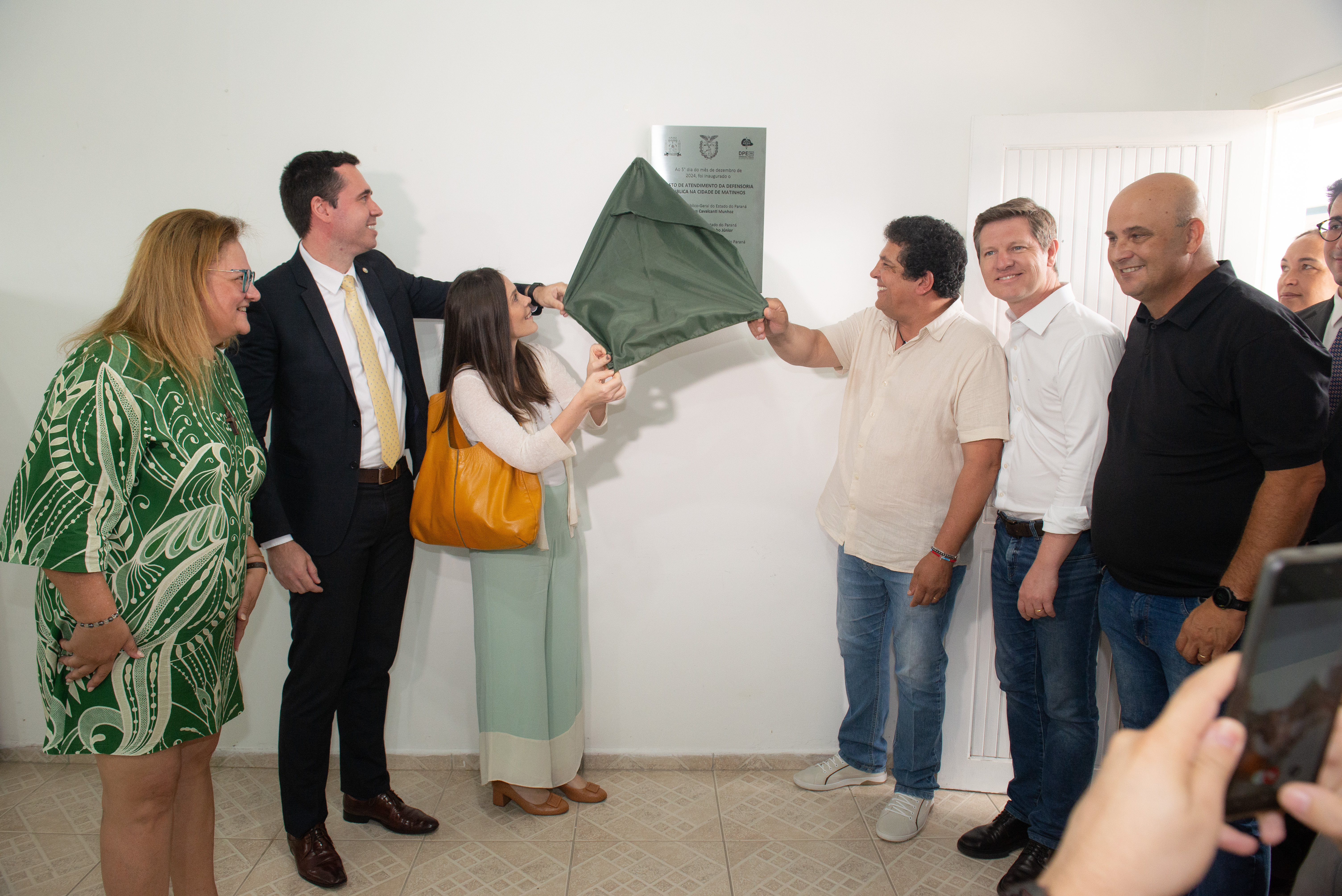 Foto colorida horizontal em que se vê autoridades descerrando a placa inaugural do Posto de Atendimento da DPE-PR em Matinhos.