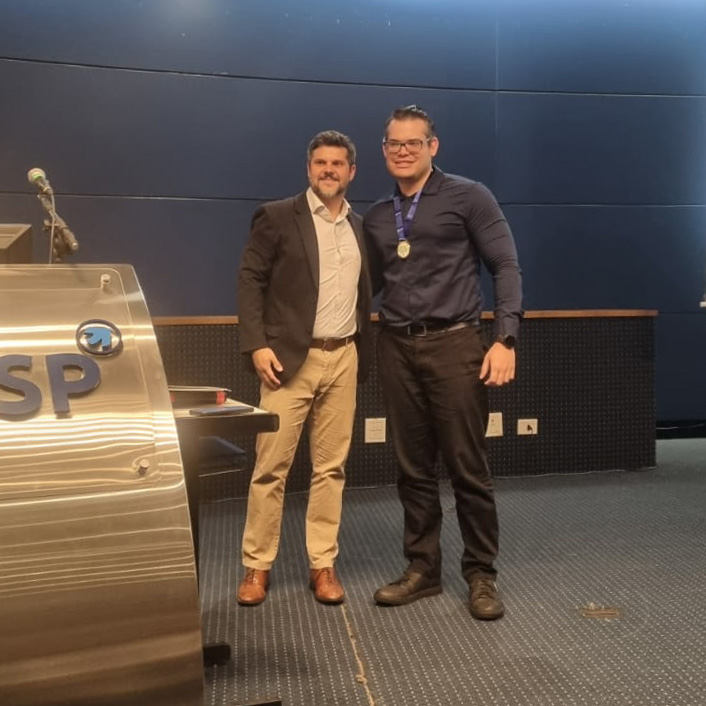 Imagem quadrada colorida em que se vê o presidente da Adepar com servidor da DPE-PR premiado.