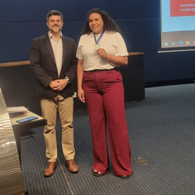 Imagem quadrada colorida em que se vê o presidente da Adepar com servidora da DPE-PR premiado.