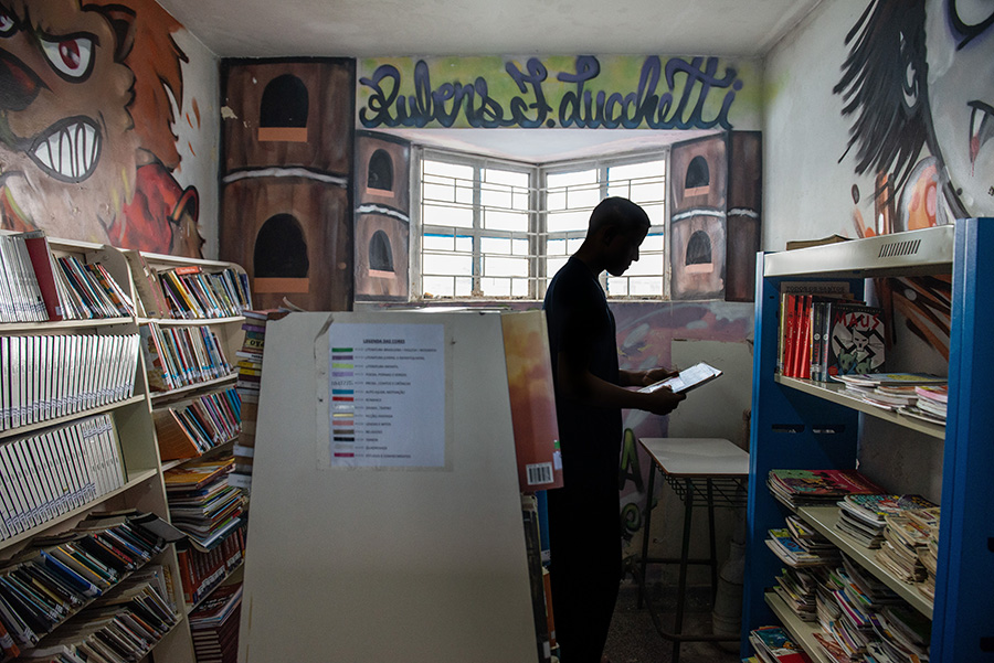 Imagem horizontal colorida em que se vê um jovem interno na biblioteca de Centro de Socioeducação. 