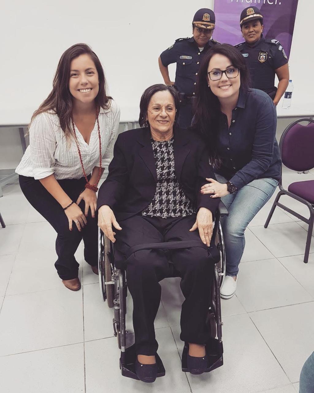 Imagem horizontal colorida em que se vê Jéssica e outra mulher posando para foto com Maria da Penha.