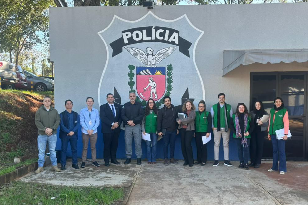 Equipe responsável pela inspeção posa para foto em frente a um muro com a logo da polícia no final do trabalho.