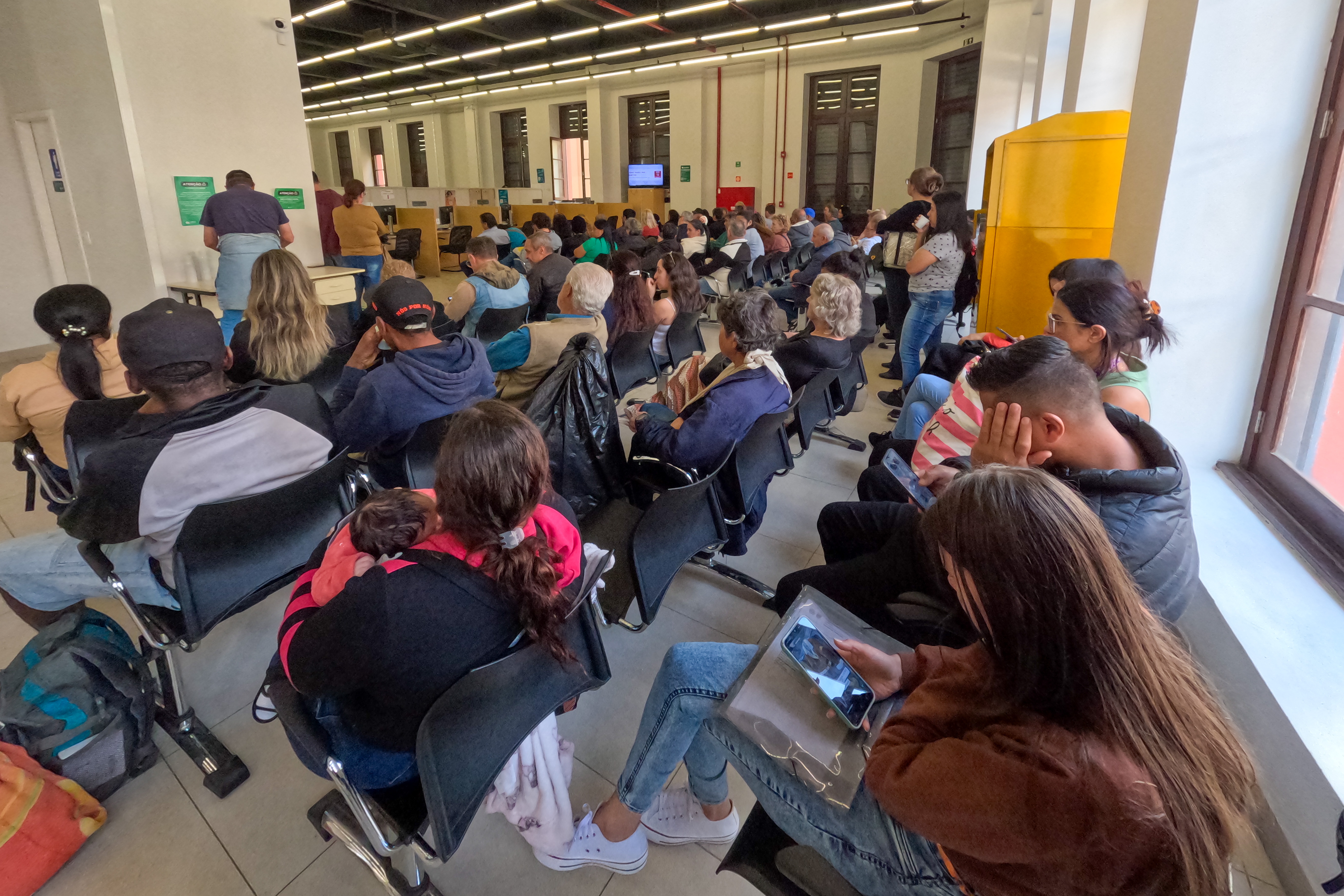 Imagem mostra aala de espera da Sede Central da Defensoria Pública com grande número de assistidos aguardando atendimento. 