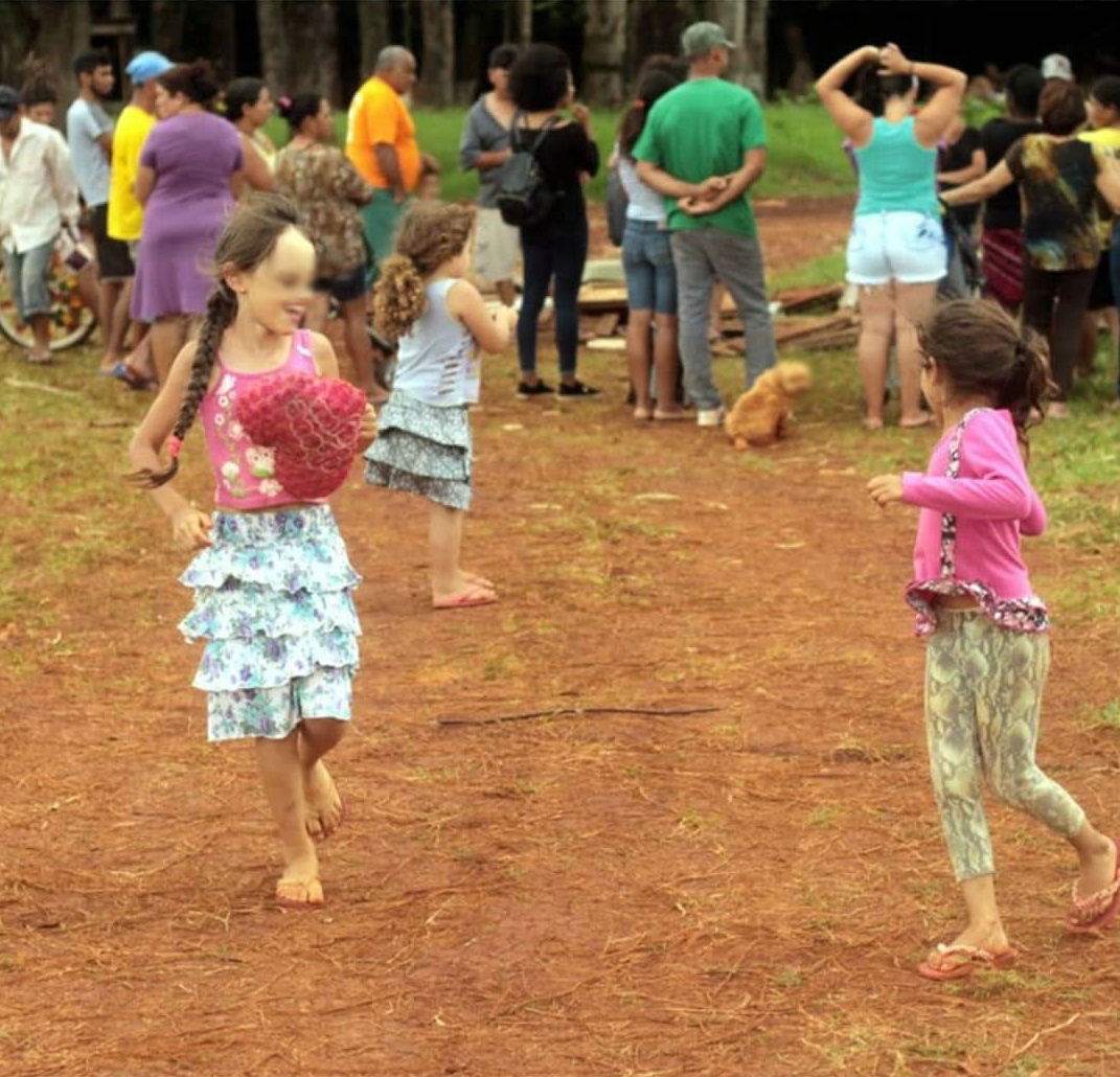 Crianças brincando, enquanto os moradores estão reunidos ao fundo.