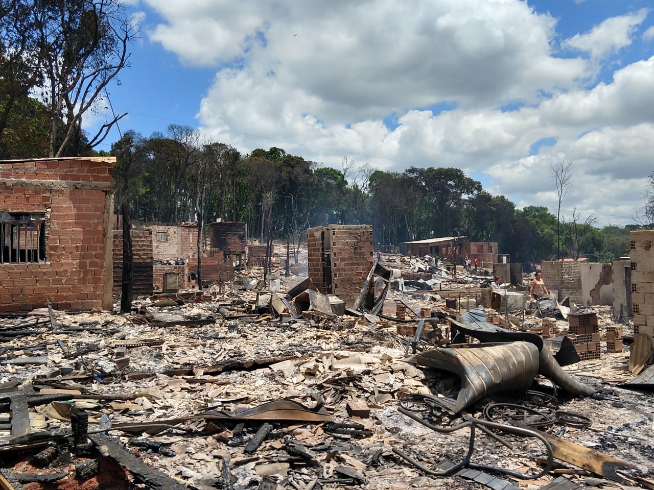 Foto mais ampla mostrando o que restou das estruturas pós incidente. Vemos muitos escombros e algumas paredes de tijolos ainda de pé.