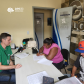 Foto de atendimento com um servidor da defensoria de pele branca camiseta verde com o logo da instituição e calça jeans, acompanhado de dois usuários assinando um documento, sendo a mulher negra com uma camisa cor de rosa e calça preta e o homem branco com calça jeans, camisa preta e boné azul com detalhes em vermelho.