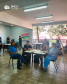 Imagem que mostra diversas pessoas aguardando atendimento no mutirão de Cascavel. Algumas pessoas estão em pé, outras estão sentadas em cadeiras, ao redor de mesas, na faculdade Unipar, onde foi realizado o evento.