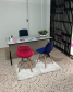Fotografia da sala de atendimento da Defensoria Pública do Estado do Paraná no Ponto de Atendimento à Mulher. A foto mostra uma mesa com a cadeira da defensora pública de um lado, e do outro duas cadeiras, uma roxa e outra rosa, onde a usuária poderá sentar.