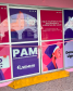 Fotografia da porta de entrada do PAM. A porta é de vidro com adesivo de artes gráficas roxa e rosa. Na frente da porta está uma fita rosa, fazendo alusão à inauguração.