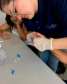 Imagem que mostra a coleta de material genético para a realização de teste de DNA. Uma funcionária do laboratório segura a mão de uma pessoa, que não aparece na imagem.