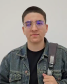 Imagem que mostra o entrevistado Diego Sikorski. Ele usa óculos, jaqueta jeans e carrega uma mochila.
