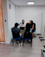 Imagem que mostra o defensor Fernando Redede e a psicóloga Lethicia Gaidarji Silva atendendo a um casal de usuários da DPE-PR, todos estão sentados em volta de uma mesa.