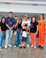Imagem da família mencionada na matéria, a foto conta com a família acompanhada da equipe que auxiliou o reencontro, eles estão posando para a foto no aeroporto.