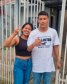 Imagem onde mostra a mãe com seu filho mais velho, ambos sorriem e posam para a foto em frente a um portão branco.