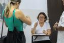 Imagem que mostra uma candidata entrando na sala de aplicação de prova, ela, que está em pé, apresenta os documentos a uma fiscal, que está sentada.