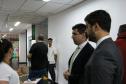 Imagem que mostra dois defensores públicos representantes da comissão organizadora do concurso conversando com uma fiscal no corredor. Atrás deles, candidatos transitam em direção às salas.