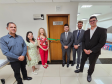 Imagem que mostra a inauguração da sala da DPE-PR em Cruzeiro do Oeste. Estão presentes a juíza diretora do Fórum, a promotora de Justiça Wilza Lacerda, o coordenador regional do Deppen, o defensor público-geral, o defensor público Pedro Bruzzi, e o 2º subdefensor-geral do estado. Todos estão ao redor da porta da sala, onde há uma placa que diz “Defensoria Pública do Estado do Paraná”. Cruzando a porta de um lado a outro há uma fita de cetim de cor verde, com um laço ao meio. Todos sorriem.