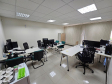 Imagem que mostra o interior da sala da DPE-PR em Cruzeiro do Oeste, onde é possível ver duas grandes mesas com computadores e cadeiras para pessoas que serão atendidas. Ao fundo, há uma grande janela, que está ocultada por uma persiana.