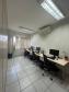 Imagem que mostra a sala de atendimento da DPE-PR em Jandaia do Sul, onde há uma mesa comprida, com 3 computadores com teclados e mouses, e 3 cadeiras. Na parede, acima da mesa, há um aparelho de ar condicionado. Ao fundo, há uma janela com uma cortina entreaberta. 