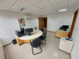 Imagem que mostra uma das salas da DPE-PR no Fórum de Cambé, onde há uma mesinha com um computador e, ao lado, mais ao centro da sala, uma mesa maior, redonda, com um computador com dois monitores e cadeiras ao redor, para receber pessoas que serão atendidas. Na parede, acima dessa mesa maior, há um quadro com desenhos de plantas e pássaros e um aparelho de ar condicionado.