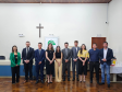 Imagem que mostra representantes da Defensoria e autoridades convidadas na inauguração da sala da DPE-PR em Jandaia. As pessoas, 4 mulheres e 6 homens, estão lado a lado e sorriem. Elas estão em uma sala ampla do Fórum, onde foi realizada a solenidade. Atrás delas é possível ver um banner com o logo da Defensoria e um crucifixo. 