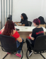 Imagem que mostra duas pessoas sendo atendidas no mutirão em Ponta Grossa. Elas estão de costas e entre elas, é possível ver a pessoa que está fazendo o atendimento, sentada atrás da mesa e olhando para a tela do computador.