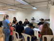Imagem com a foto de usuários e usuárias da Defensoria recebendo o atendimento sentamos em cadeiras e mesas brancas dentro de uma sala. 