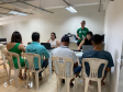 Imagem com a foto de usuários e usuárias da Defensoria recebendo o atendimento sentamos em cadeiras e mesas brancas dentro de uma sala. 
