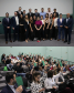 Imagem com a colagem de duas fotos. Na primeira, acima, temos uma foto dos novos defensores que finalziam o curso de formação. Na imagem abaixo, uma foto dos defensores votando para aprovação ou não de uma tese apresentada no evento.