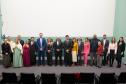 Imagem horizontal colorida em que se vê todos os presentes na cerimônia de posse dos Novos Defensores posando juntos no auditório. 