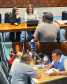 Imagem em formato de colagem entre duas fotos, a primeira, na parte de cima, tem duas moças atendendo um usuário da Defensoria Pública. Na foto de baixo, uma foto da capa onde um atendente conversa com um casal de idosos.