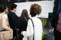 Imagem horizontal colorida que mostra os candidatos conferindo seus locais de provas no mural.