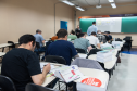 Imagem horizontal colorida que mostra os candidatos realizando as provas. 