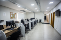 Sala ampla e bem iluminada com várias mesas de atendimento organizadas em fileiras, cada uma equipada com computador e cadeiras para os atendentes e assistidos; ao fundo, um corredor leva a outras salas.