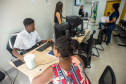 Atendimento ao público no interior da Defensoria, com servidores auxiliando cidadãos em balcões de recepção, em um ambiente iluminado e organizado.