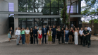 Autoridades e servidores da Defensoria Pública posam para foto na frente do prédio, vestindo trajes formais. Alguns seguram documentos e faixas comemorativas.