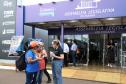 Imagem colorida horizontal em plano aberto em que se vê duas moças recebendo um panfleto de uma moça com informações sobre os serviços da DPE-PR durante o evento Assembleia Itinerante realizado em Londrina.