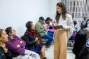 Imagem colorida horizontal em que se vê servidora da DPE-PR entregando as senhas e fazendo a orientação dos assistidos. 