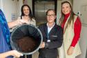 Três mulheres posam com a borra de café na sede da Defensoria. Toda borra do café passado na instituição será entregue no Ecoponto da Prefeitura de Curitiba onde vira adubo em um minhocário.   