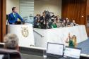 Em primeiro plano a mesa diretiva da ALEP-PR, ao fundo Defensor Público Geral discursa na Tribuna e representantes da instituição acompanham a sessão do primeiro balcão. 
