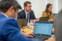 A imagem mostra pessoa de costas em primeiro plano e ao fundo se vê um homem e uma mulher; todos estão usando laptops.