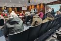 Um grupo grande pessoas, algumas sentadas outras em pé, aguardam o atendimento da Defensoria Pública do Paraná durante o Mutirão na ALEP. Ao fundo os atendimentos. 