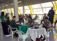 Imagem mostra um grande grupo de pessoas, algumas em pé, outras sentadas à mesa, em mutirão da Defensoria realizado em terminal de ônibus.