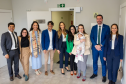 Esta é uma foto de confraternização, que reúne um grupo posando para a câmera. Estão presentes a Ouvidora-Geral, defensores da sede de Foz, o Defensor Público-Geral e a Primeira e Segunda Subdefensoras-Gerais. São dez pessoas no total, além de um bebê no colo de uma das participantes. Todos sorriem em um corredor do novo prédio, onde uma placa na parede identifica o local: "DEFENSORIA PÚBLICA DO ESTADO DO PARANÁ".
